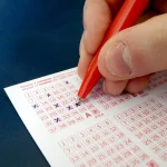 A hand filling in a lottery ticket with a pen