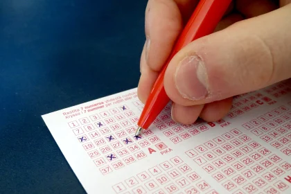 A hand filling in a lottery ticket with a pen