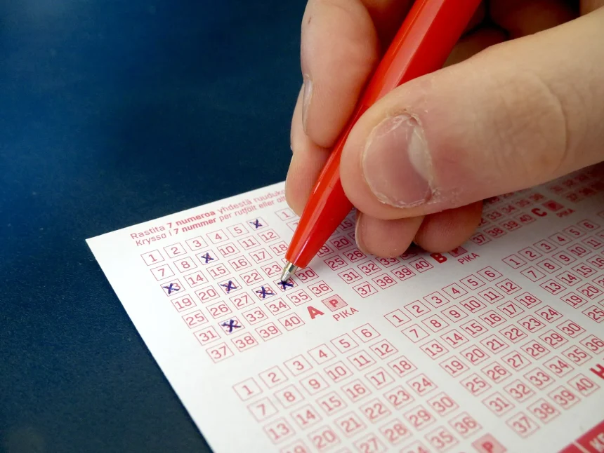 A hand filling in a lottery ticket with a pen