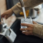A person filling a glass with water at a kitchen sink tap