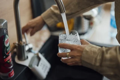 A person filling a glass with water at a kitchen sink tap
