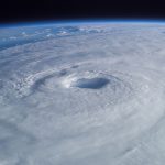 A weather satellite orbiting above Earth with swirling cloud systems below